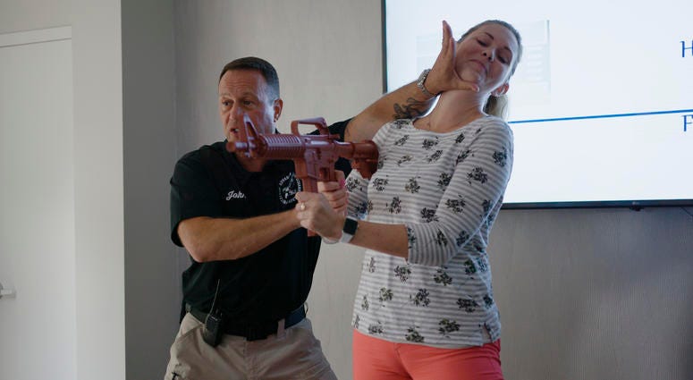 In this July 17, 2019 photo provided by Market Mentors, LLC, John Nettis from PASS, left, demonstrates techniques for fighting with Amanda Moyer, director of account services at Market Mentors at the Market Mentors office in Springfield, Mass. Gun safety defense demonstration