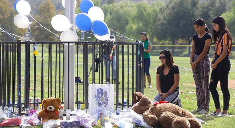Parent Mirna Herrera kneels with her daughters Liliana, 15, and Alexandra, 16 at the Central Park memorial for the Saugus High School victims in Santa Clarita, Calif., Friday, Nov. 15, 2019. Parent Mirna Herrera kneels with her daughters Liliana, 15, and Alexandra, 16 at the Central Park memorial for the Saugus High School victims in Santa Clarita.
