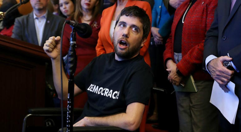 Ady Barkan, who lives with Amyotrophic Lateral Sclerosis, delivers remarks during a rally organized by House Minority Leader Nancy Pelosi (D-CA) in the Rayburn Room at the U.S. Capitol December 19, 2017 in Washington, DC. Ady Barkan, who lives with Amyotrophic Lateral Sclerosis, delivers remarks during a rally organized by House Minority Leader Nancy Pelosi (D-CA) in the Rayburn Room at the U.S. Capitol December 19, 2017 in Washington, DC.