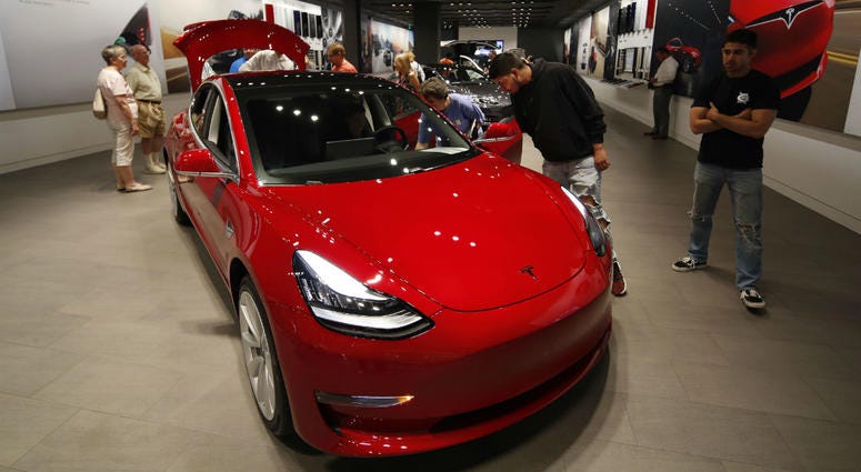 In this July 6, 2018, file photo prospective customers confer with sales associates as a Model 3 sits on display in a Tesla showroom in the Cherry Creek Mall in Denver. In this July 6, 2018, file photo prospective customers confer with sales associates as a Model 3 sits on display in a Tesla showroom in the Cherry Creek Mall in Denver.