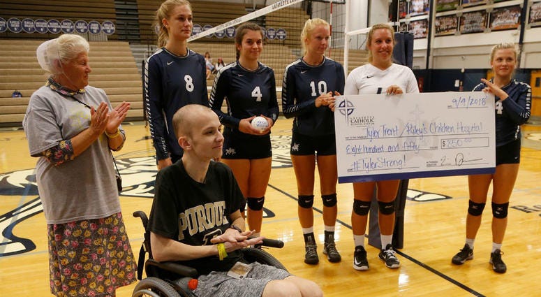 In this Tuesday, Sept. 4, 2018, photo, Central Catholic players present Tyler Trent, foreground, with a check to benefit Riley Children's Hospital before meeting Lafayette Jeff in a high school volleyball game, in Lafayette, Ind. In this Tuesday, Sept. 4, 2018, photo, Central Catholic players present Tyler Trent, foreground, with a check to benefit Riley Children's Hospital before meeting Lafayette Jeff in a high school volleyball game, in Lafayette, Ind.