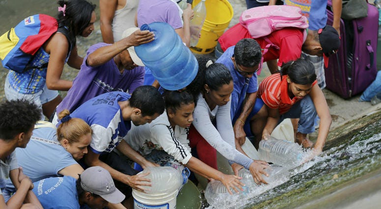 People collect water from an open pipe above the Guaire River during rolling blackouts, which affects the water pumps in people's homes, offices and stores, in Caracas, Venezuela, Monday, March 11, 2019. People collect water from an open pipe above the Guaire River during rolling blackouts, which affects the water pumps in people's homes, offices and stores, in Caracas, Venezuela, Monday, March 11, 2019.