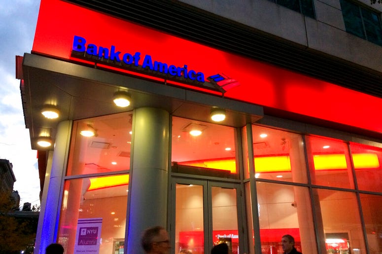 FILE- In this Nov. 6, 2017, file photo, people walk by a branch office of Bank of America in New York. Bank of America is raising its starting pay to $20 an hour over a two-year period, starting with a hike next month. The company said Tuesday, April 9, 2