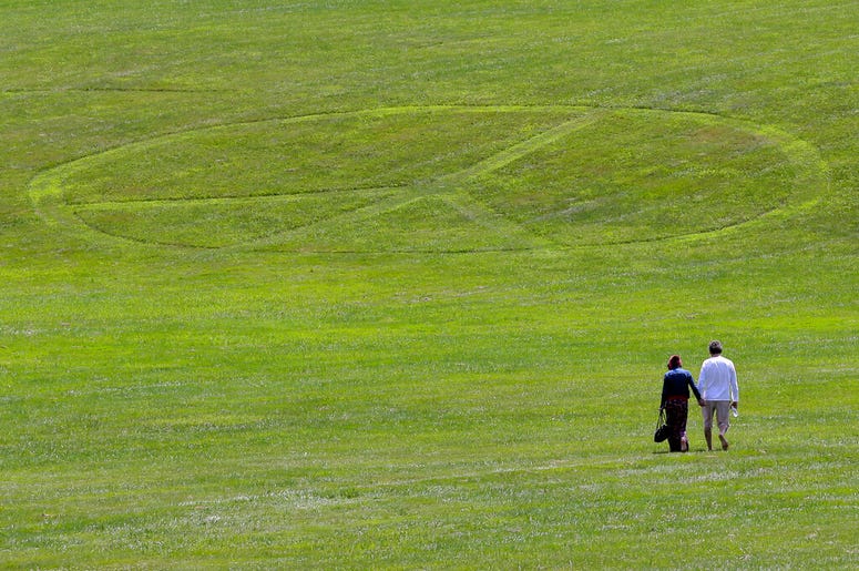 Carol Laura, left, and George Acquaire walk barefoot to a peace sign mowed in the grass at the site of the 1969 Woodstock Music and Arts Fair, Wednesday, July 24, 2019 in Bethel, N.Y. Woodstock will be celebrated on its 50th anniversary, but it won't be y