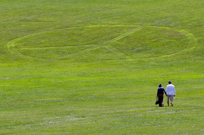 Carol Laura, left, and George Acquaire walk barefoot to a peace sign mowed in the grass at the site of the 1969 Woodstock Music and Arts Fair, Wednesday, July 24, 2019 in Bethel, N.Y. Woodstock will be celebrated on its 50th anniversary, but it won't be y