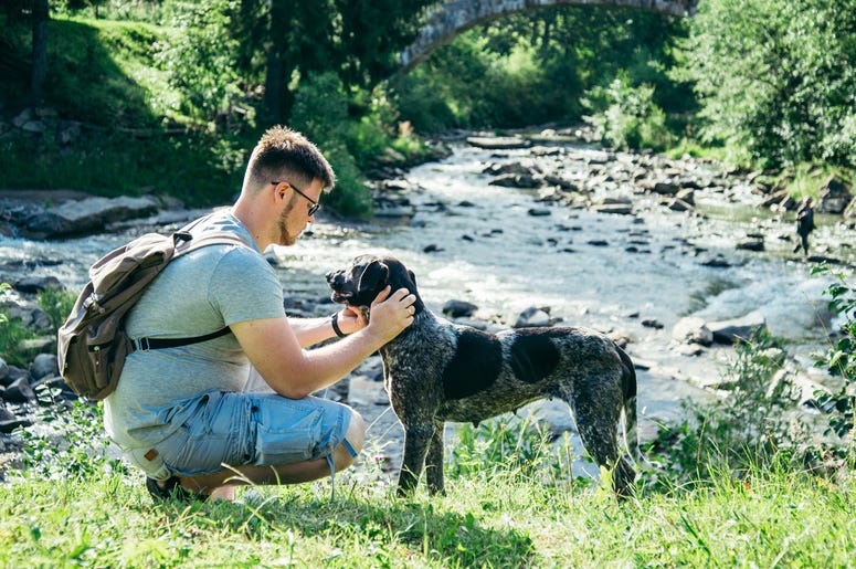 Young strong man with backpack stays near mountains river with dog and looking for the view. Young strong man stays near mountains river with dog and looking for the view. Fidelity, life.