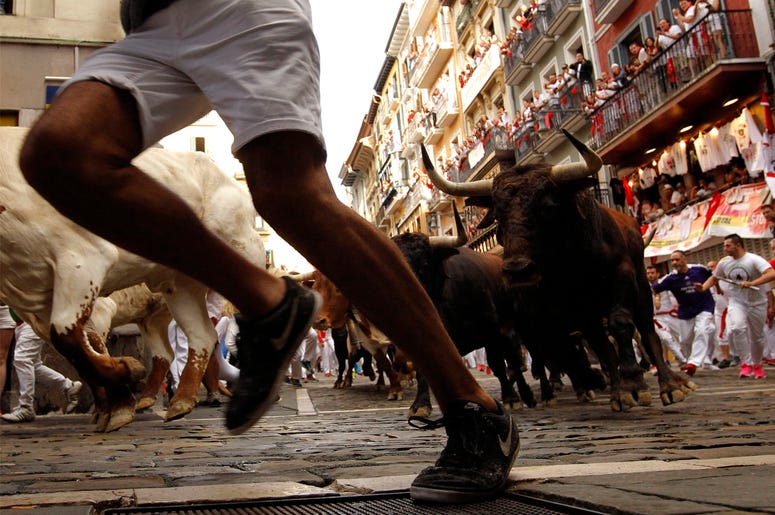 AP19189231643904 Revellers run next to fighting bulls from Cebada Gago ranch, during the running of the bulls at the San Fermin Festival, in Pamplona, northern Spain, Monday, July 8, 2019. Revellers from around the world flock to Pamplona every year to take part in the ei