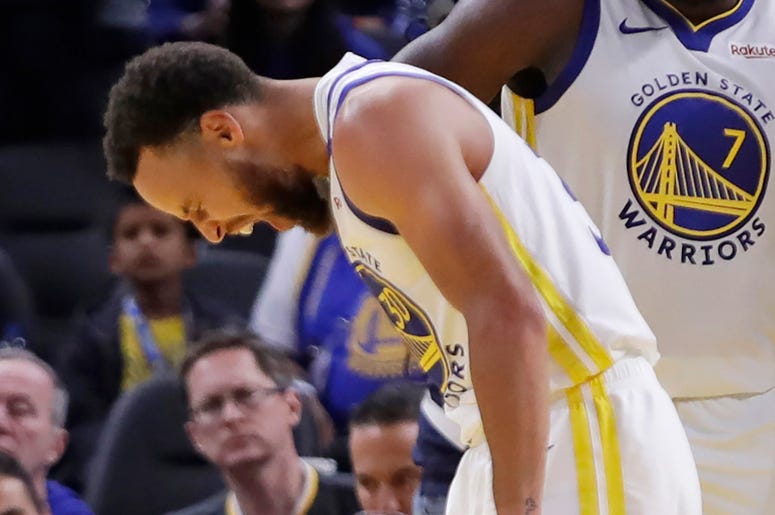 AP19304160060069 Golden State Warriors' Stephen Curry, left, grimaces as Eric Paschall (7) and Glenn Robinson III (22) watch, after Phoenix Suns' Aron Baynes fell onto Curry during the second half of an NBA basketball game Wednesday, Oct. 30, 2019, in San Francisco. Curry