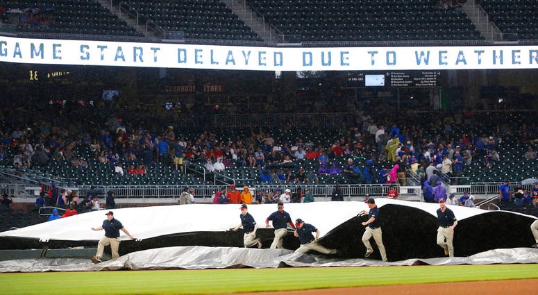 Members of the Atlanta Braves grounds crew rush to cover the infield during a rain shower before the Braves' baseball game against the Chicago Cubs on Thursday, May 17, 2018, in Atlanta.