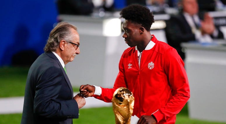 Decio de Maria, President of the Football Association of Mexico, left, and Canadian soccer player Alphonso Davies, right, present a joint United bid by Canada, Mexico and the United States to host the 2026 World Cup