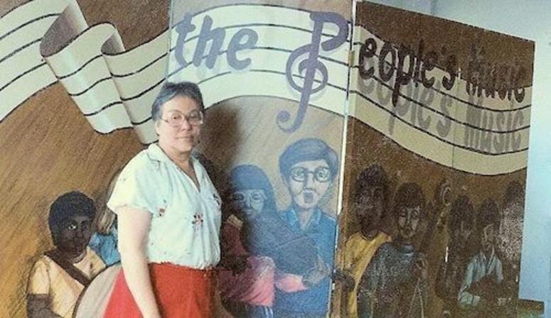 Rita Simó shown in front of a banner from the early days of The People's Music School