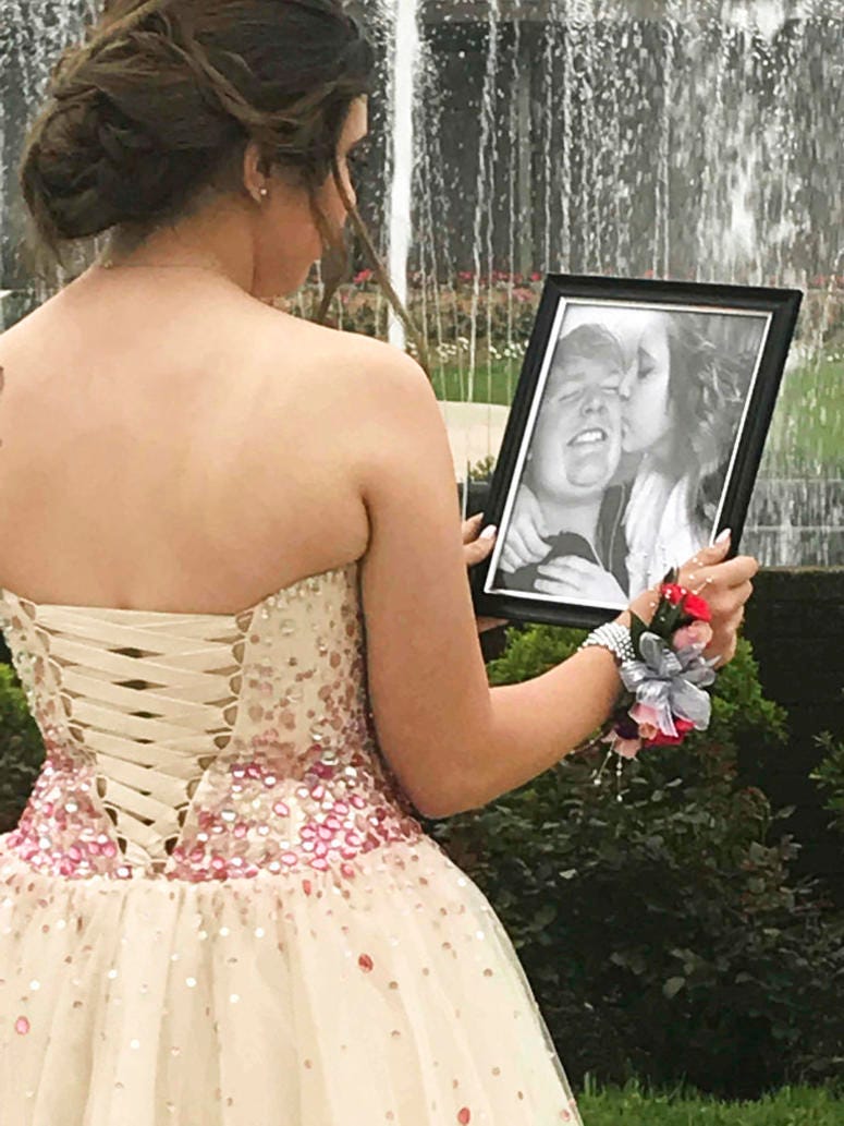 In this Saturday, May 19, 2018, photo provided by Kelly Brown, James Buchanan High School senior Kaylee Suders looks at a picture of her kissing her boyfriend Carter Brown, who died in a car wreck last month.