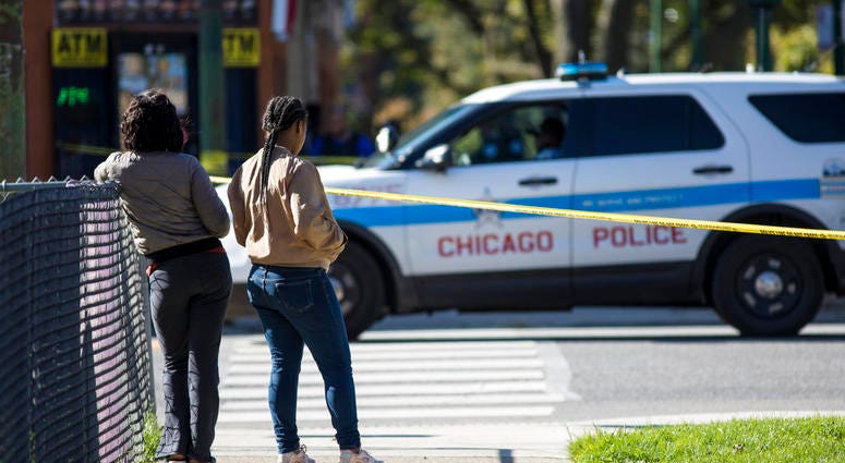 In this Monday, Oct. 22, 2018 photo, residents watch as Chicago Police investigate following a shooting after a funeral service in Chicago. Police scrambled Tuesday to ward off retaliatory attacks by street gangs after a Chicago rapper known for taunting In this Monday, Oct. 22, 2018 photo, residents watch as Chicago Police investigate following a shooting after a funeral service in Chicago. Police scrambled Tuesday to ward off retaliatory attacks by street gangs after a Chicago rapper known for taunting