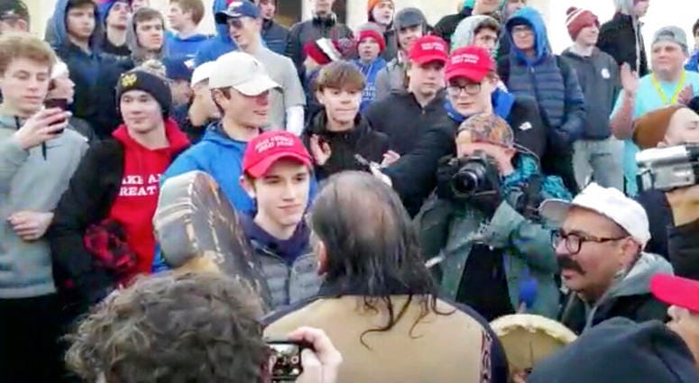 In this Friday, Jan. 18, 2019 image made from video provided by the Survival Media Agency, a teenager wearing a "Make America Great Again" hat, center left, stands in front of an elderly Native American singing and playing a drum in Washington. The Roman In this Friday, Jan. 18, 2019 image made from video provided by the Survival Media Agency, a teenager wearing a "Make America Great Again" hat, center left, stands in front of an elderly Native American singing and playing a drum in Washington. The Roman