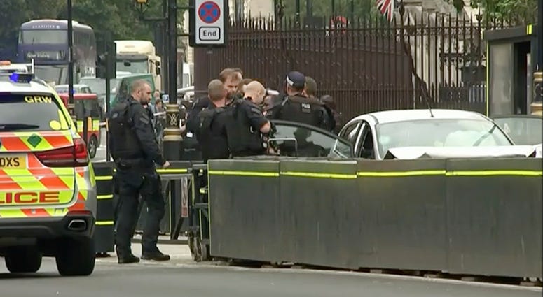 In this frame grab taken Tuesday, Aug. 14, 2018 armed police train their weapons on a car crashed into security barriers outside the Houses of Parliament stands to the right of a bus in London. London crash