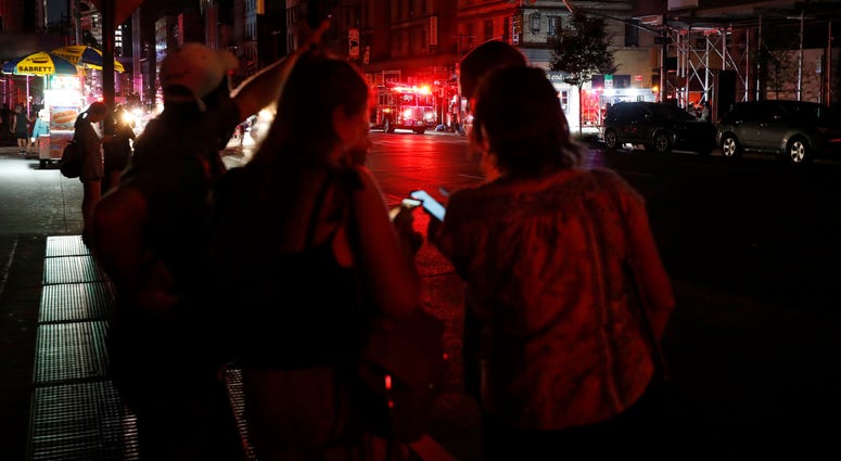 Pedestrians looks at their cellphones during a power outage in midtown Manhattan, Saturday, July 13, 2019, in New York. nyc blackout AP