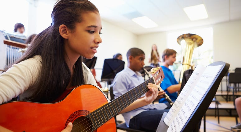 Students learn how to play instruments in a music class. High School Music Class