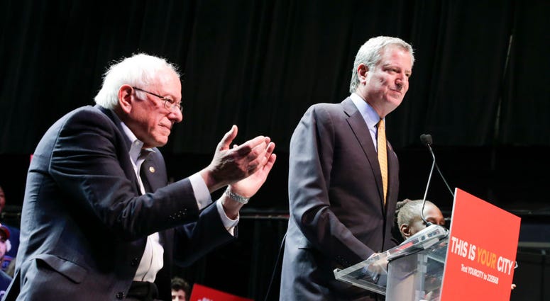 Mayor Bill de Blasio (R) speaks to supporters next to Sen. Bernie Sanders (I-VT) as they take part in a campaign rally on October 30, 2017 in New York City. Mayor Bill de Blasio and Sen. Bernie Sanders