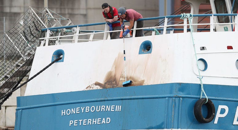 Members of the crew clean marks from the stern of the Honeybourne III, a Scottish scallop dredger, whilst in dock at Shoreham, West Sussex, following clashes with French fishermen in the English Channel. Scallop Ship