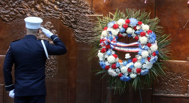 A member of the honor guard salutes the wreath hung at the memorial outside the building that houses Fire Co. 10