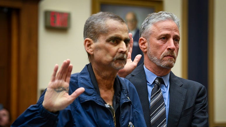 Jon Stewart helps Luis Alvarez, Detective (Ret.) and 9/11 Responder, New York Police Department, as they are sworn before testimony in front of the House Judiciary Committee. Lou Alvarez, Jon Stewart