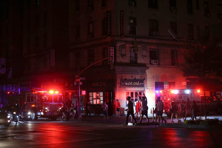 Pedestrians cross the street near emergency response vehicles at 50th Street and 8th Avenue during a power outage, Saturday, July 13, 2019, in New York. NYC blackout AP