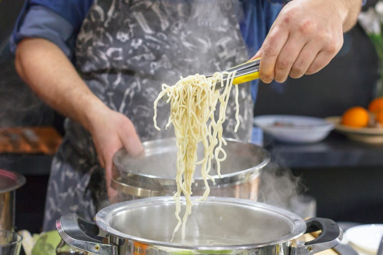 Chef takes out with slotted spoon hot steaming noodles from the pan Italian cooking class