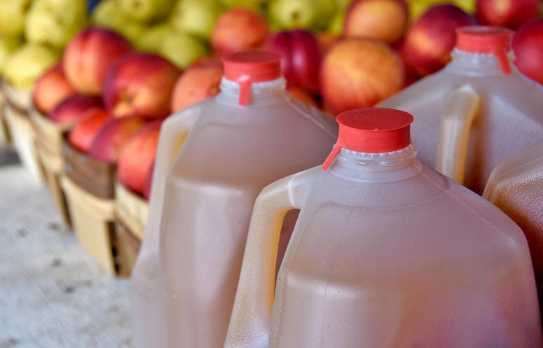 Autumn apple cider in plastic gallon jugs with apples at the market Apple Cider