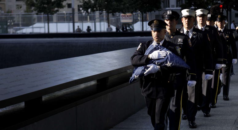 Police and firefighters march in formation and carry a folded flag past a memorial pool at the National September 11 Memorial. 9/11 Memorial