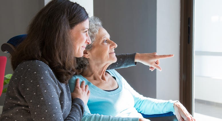 Happy senior mother and adult daughter enjoying dramatic view out of window. Elderly lady resting in armchair, while young woman pointing out of window. Happy senior mother and adult daughter enjoying dramatic view out of window. Elderly lady resting in armchair, while young woman pointing out of window.