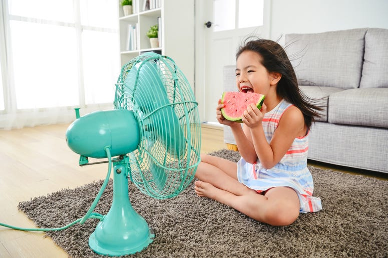 child eating watermelon with two hands. sitting in front of the electric fan child eating watermelon with two hands. sitting in front of the electric fan
