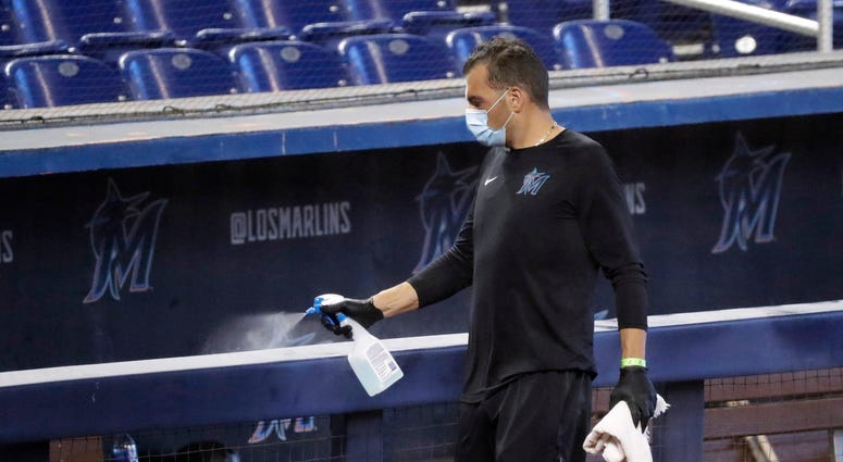 A worker sprays the dugout rail to help prevent the spread of the coronavirus, before the Miami Marlins' baseball practice at Marlins Park in Miami. The Marlins, one of the most under-the-radar teams in sports, have making news lately, all of it bad.