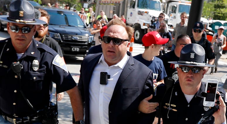 In this Tuesday, July 19, 2016 file photo, Alex Jones, center right, is escorted by police out of a crowd of protesters outside the Republican convention in Cleveland. In this Tuesday, July 19, 2016 file photo, Alex Jones, center right, is escorted by police out of a crowd of protesters outside the Republican convention in Cleveland.