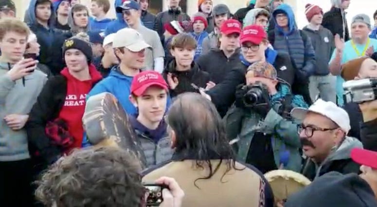 Media Agency, a teenager wearing a "Make America Great Again" hat, center left, stands in front of an elderly Native American singing and playing a drum in Washington. MAGA hat Native American Washington