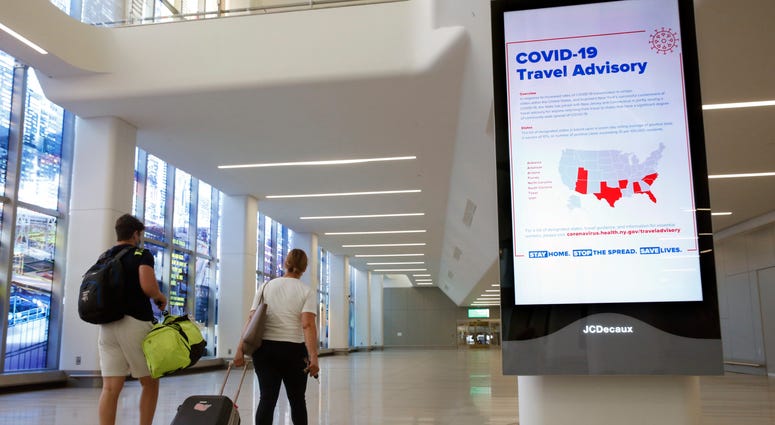In this June 25, 2020, file photo, arriving travelers walk by a COVID-19 travel advisory sign in the baggage claim area of Terminal B at New York City's LaGuardia Airport. Coronavirus NYC