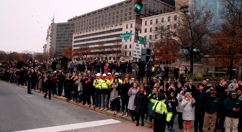) People watch as the hearse carrying the flag-draped casket of former President George H.W. Bush passes Freedom Plaza on its way to a State Funeral at the National Cathedral December 5, 2018 in Washington, DC. George H.W. Bush
