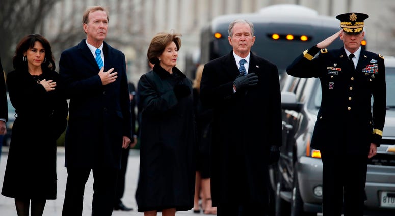 From right, former President George W. Bush, second from right, former first lady Laura Bush, Neil Bush and Sharon Bush, stand as the flag-draped casket of former President George H.W. Bush is carried by a joint services military honor guard. George H.W. Bush