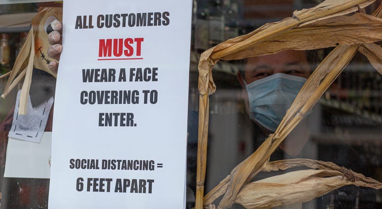 A worker places a placard on the window of a liquor store while wearing a face mask on April 10, 2020 in Jersey City, New Jersey.