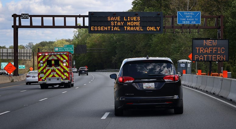 An ambulance speeds past Maryland Cremation Services employees Emma Tilghman and Morgan Dean-McMillan's vehicle as they transport a coronavirus victim on the highway underneath a digital billboard telling people to stay home May 11, 2020 in Germantown, Ma Coronavirus sign