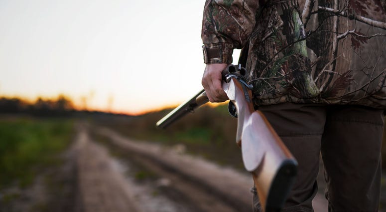 A hunter with a rifle walking on a dirt road. A hunter with a rifle walking on a dirt road.