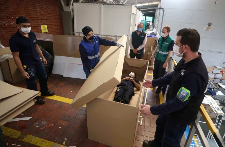 Rodolfo Gomez, to center, and his employees demonstrate how their design of a cardboard box can serve as both a hospital bed and a coffin, designed for COVID-19 patients, in Bogota, Colombia, Friday, May 8, 2020. Hospital bed coffins