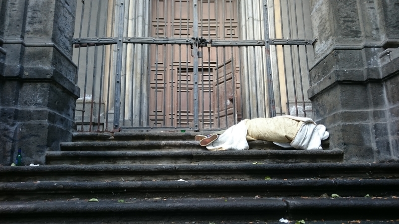A homeless person sleeps on the steps of a church. A homeless person sleeps on the steps of a church.
