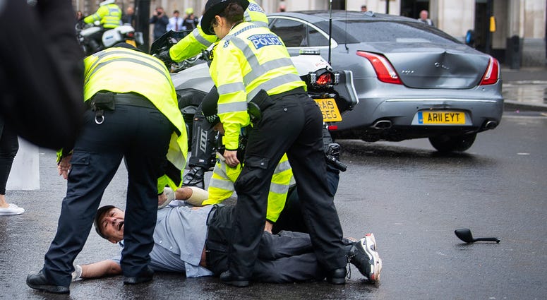 Police detain a man after he ran in front of Prime Minister Boris Johnson's car (in background with dent) as it left the Houses of Parliament, Westminster. Boris Johnson car crash