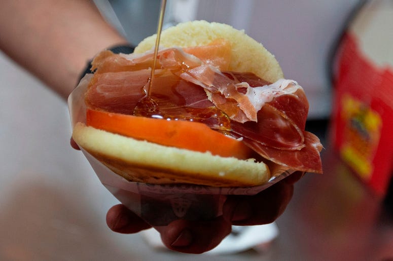 En esta imagen del 19 de junio de 2019, el cocinero y propietario del restaurante Arepa Olé, Edgar Rodr guez, de Venezuela, prepara una Arepa Iberia con jamón serrano, tomate y aceite de oliva en Madrid, España. En esta imagen del 19 de junio de 2019, el cocinero y propietario del restaurante Arepa Olé, Edgar Rodr guez, de Venezuela, prepara una Arepa Iberia con jamón serrano, tomate y aceite de oliva en Madrid, España.
