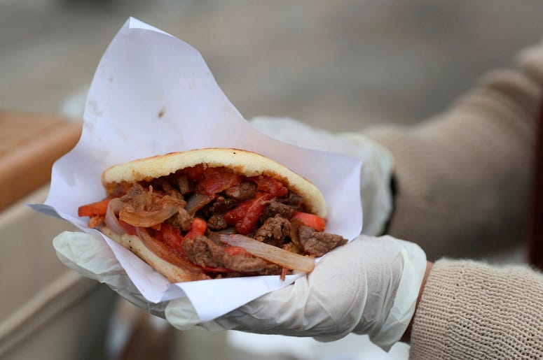 En esta imagen del 12 de junio de 2019, la vendedora venezolana de arepas Yuleiny Mendoza muestra una de sus creaciones de comida callejera en una esquina en Lima, Perú. En esta imagen del 12 de junio de 2019, la vendedora venezolana de arepas Yuleiny Mendoza muestra una de sus creaciones de comida callejera en una esquina en Lima, Perú.