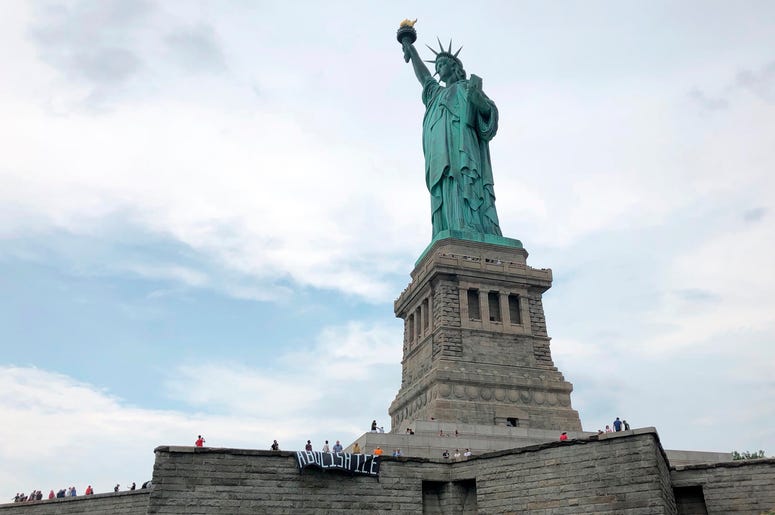 En esta fotografía difundida por el grupo Rise and Resist, varios manifestantes despliegan una carta que pide abolir el Servicio de Control de Inmigración y Aduanas de Estados Unidos (ICE por sus siglas en inglés) en la base de la Estatua de la Libertad. En esta fotografía difundida por el grupo Rise and Resist, varios manifestantes despliegan una carta que pide abolir el Servicio de Control de Inmigración y Aduanas de Estados Unidos (ICE por sus siglas en inglés) en la base de la Estatua de la Libertad.