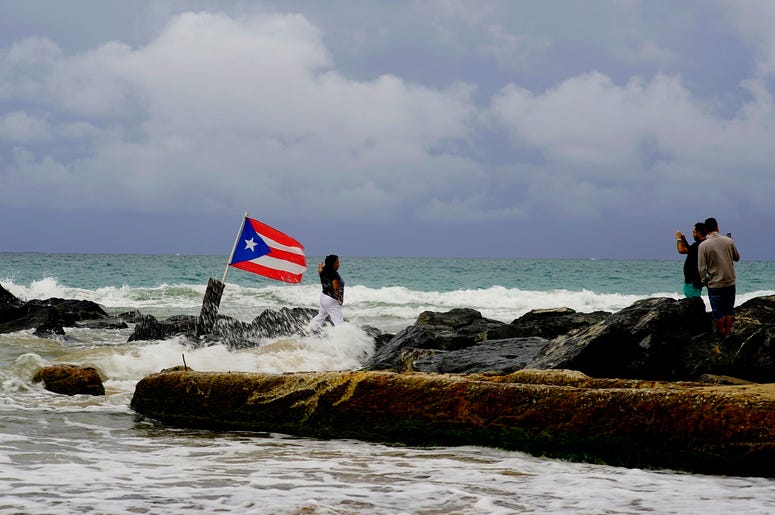 Una mujer posa para una fotografía con el mar y una bandera de Puerto Rico de fondo tras el paso de la tormenta tropical Dorian por la isla, en San Juan, Puerto Rico, el 28 de agosto de 2019. Una mujer posa para una fotografía con el mar y una bandera de Puerto Rico de fondo tras el paso de la tormenta tropical Dorian por la isla, en San Juan, Puerto Rico, el 28 de agosto de 2019.
