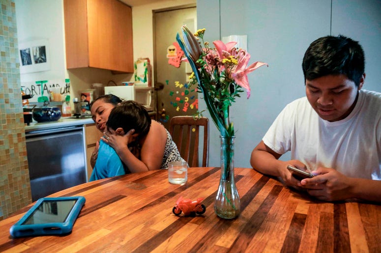 la inmigrante guatemalteca Rosayra Pablo Cruz, a la izquierda, consuela a su hijo menor Fernando, de 6 años, con un abrazo, mientras que Yordy, de 17 años, usa su teléfono celular en la cocina de la planta baja de su hogar de acogida en Nueva York. la inmigrante guatemalteca Rosayra Pablo Cruz, a la izquierda, consuela a su hijo menor Fernando, de 6 años, con un abrazo, mientras que Yordy, de 17 años, usa su teléfono celular en la cocina de la planta baja de su hogar de acogida en Nueva York.