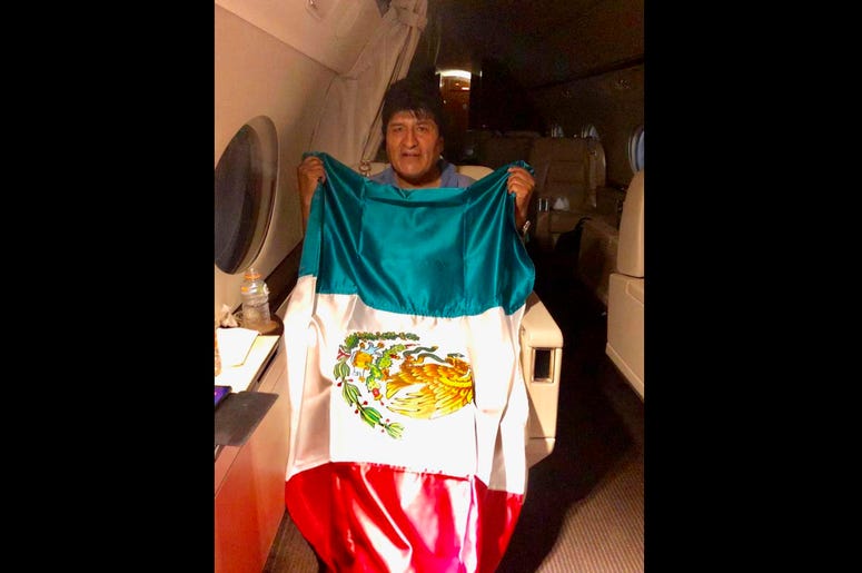 En esta imagen publicada por el ministro mexicano de Exteriores, Marcelo Ebrard, se ve al expresidente de Bolivia Evo Morales sosteniendo una bandera mexicana a bordo de un avión de la Fuerza Aérea mexicana, el lunes 11 de noviembre de 2019. protests. En esta imagen publicada por el ministro mexicano de Exteriores, Marcelo Ebrard, se ve al expresidente de Bolivia Evo Morales sosteniendo una bandera mexicana a bordo de un avión de la Fuerza Aérea mexicana, el lunes 11 de noviembre de 2019. protests.