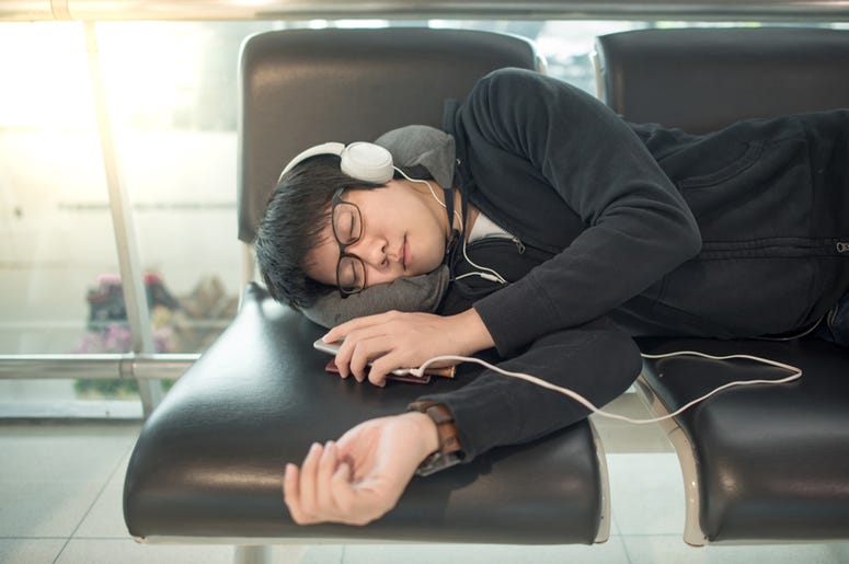 man asleep on a suitcase at the airport